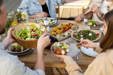  Pessoas reunidas à mesa compartilhando saladas e alimentos saudáveis em um almoço.