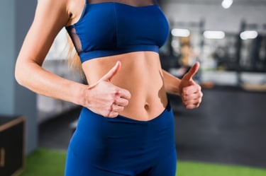 Mulher em roupa fitness azul mostrando abdômen definido e fazendo sinal de positivo com as duas mãos