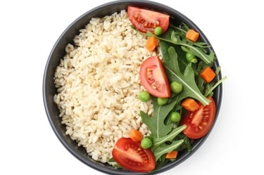 Top view of a healthy bowl of brown rice with fresh tomatoes, arugula, peas, and carrots.
