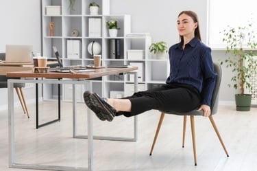 A woman performing leg extensions as office exercises while sitting at her desk in a modern workspace.