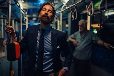 A businessman in a navy suit standing on a public bus during a night commute.