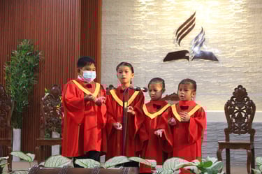 Little kids wearing red church robe singing on a stage