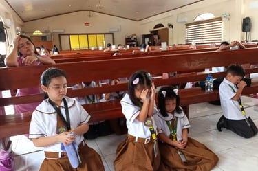 Elementary students praying in a school chapel on a wooden church bench