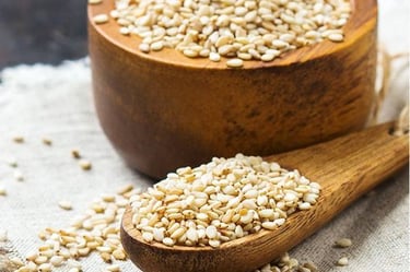 a wooden spoon with sesame seeds and a wooden bowl with sesame seeds