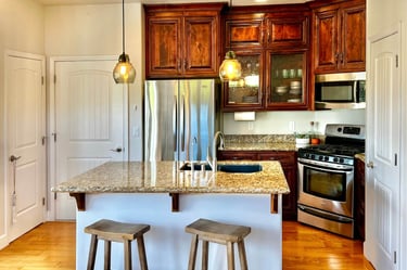 A kitchen with a warm wood cabinet stain, glowing granite countertops, and hand scraped wood floors.