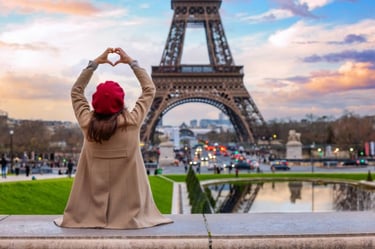 A woman in a red beret making a heart shape with her hands in front of the Eiffel Tower in Paris.