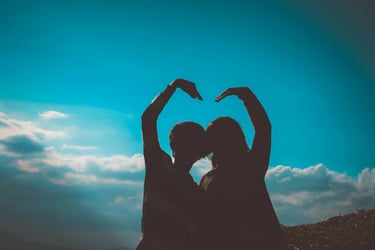 deux silhouettes regardant l'horizon bleu et formant un coeur avec leurs bras