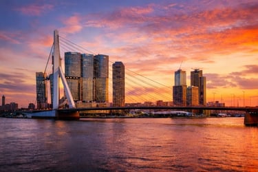 Rotterdam skyline and Erasmus Bridge at sunset with vibrant orange clouds over the Maas river.