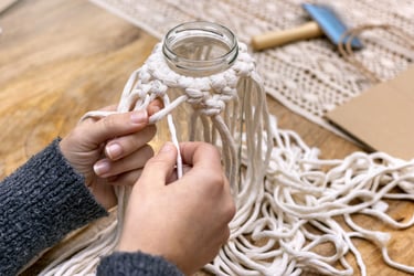 Manos haciendo nudo cuadrado con cordón de algodón para crear funda macramé casera hoy.