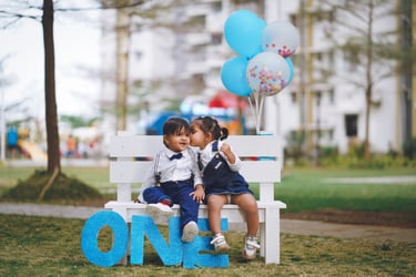 "A baby taking their first steps on the grass while holding a parent's hand."