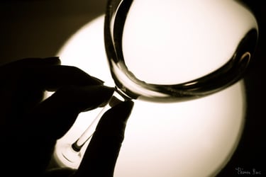 Vue en gros plan d’un verre de vin de profil, avec des doigt qui tiennent le pied du verre.