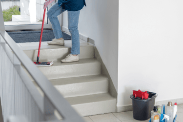 Limpiadora en una escalera con pasillos, limpiando el suelo con una fregona.