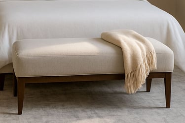Bedroom with a bench at the foot of the bed, styled in soft lighting with neutral tones and subtle shadows.