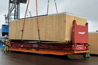 A red 40ft flat rack being loaded with a large wooden container