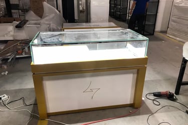 Custom lighted glass jewelry display case with gold trim in a retail manufacturing warehouse.