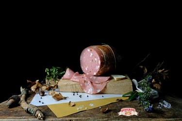 Sliced Italian mortadella deli meat on a wooden board with herbs and peppercorns on a black background.