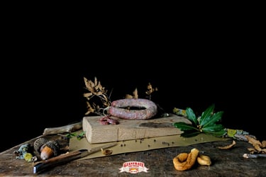 Artisanal Italian cured sausage on a rustic wooden cutting board with bay leaves and peppercorns.