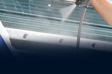 Professional technician cleaning air conditioner evaporator coils with a high-pressure water spray tool.