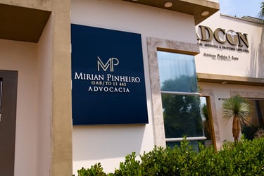 Modern blue signage for Mirian Pinheiro Advocacia law firm on a building exterior with green shrubs.