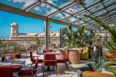 Luxury rooftop restaurant with a glass ceiling and views of a historic stone fortress under a clear blue sky.