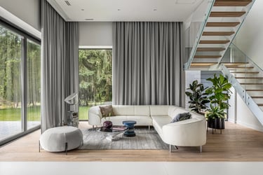 Przestronny salon z białym narożnikiem, szklane schody i widok na las przez wysokie okna.