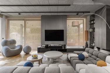 Przestronny salon, szara modułowa sofa, designerski fotel w pasy i drewniana podłoga jodła.