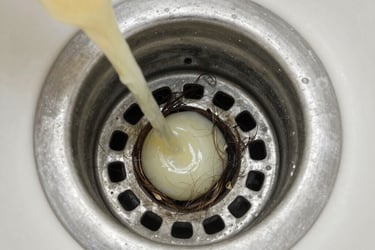 Liquid drain cleaner pouring into a clogged sink drain filled with hair and residue.