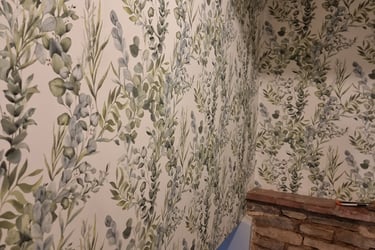 Top of a staircase with pale, vine-like wallpapered walls leading downstairs, in a residential home.