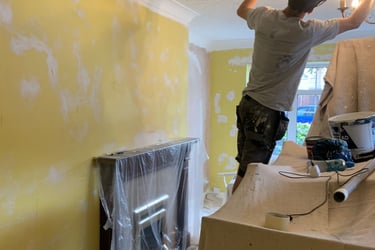 An in-progress living room, with sheet covered furniture and a painter reaching to the ceiling.
