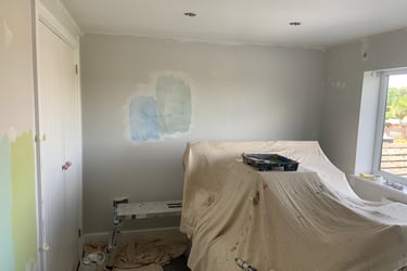An in-progress bedroom, with sheet covered furniture and evidence of paint-testing on the walls.