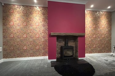 A painted burgundy fireplace, with surrounding brown, botanical wallpaper.