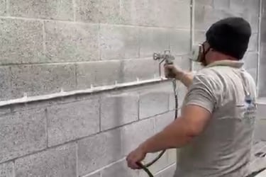 LPAD staff using a paint sprayer on an industrial cinderblock wall.