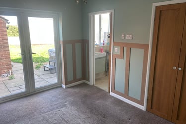 An unfurnished room with grey, painted walls and wooden rectangular detailing on the lower half.