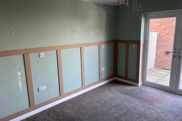 An unfurnished room with grey, painted walls and wooden rectangular detailing on the lower half.