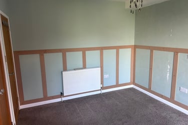 An unfurnished room with grey, painted walls and wooden rectangular detailing on the lower half.