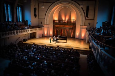 Musicians performing a classical concert on stage with a grand piano in a crowded theater venue.