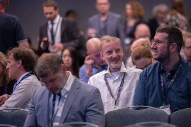 A smiling professional man sitting in a crowded conference room during a business seminar.