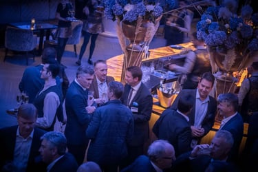 Business professionals networking at a sophisticated cocktail event with blue flowers and an elegant bar.