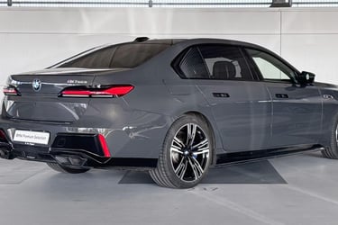 Rear view of a dark grey BMW M760e luxury plug-in hybrid sedan in a showroom.