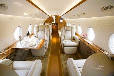 Luxury private jet interior featuring beige leather seats and a wooden dining table.