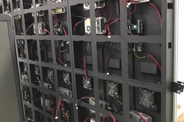 Rear view of an outdoor LED video wall display showing modular power supplies, cooling fans, and wiring.