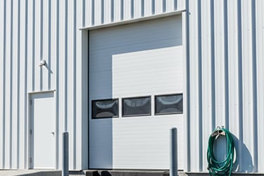 White industrial warehouse loading dock with a sectional overhead door and metal siding.