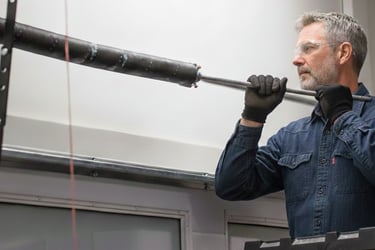 Professional technician on a ladder installing a heavy-duty garage door torsion spring.