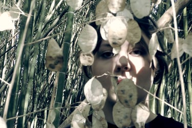 Film still from "As I Bury My Face Into My Hands" by Tina Bikic of a face partly hidden among tall plants.