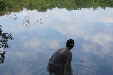 Film still from "Fear" by Tina Bikic showing a swimmer in a dark cap facing the water’s reflection, with clouds mirrored.
