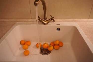 Film still from The Wait by Tina Bikic showing oranges in a white sink under running water from a brass tap.