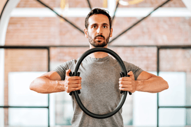 Man with brown hair using a pilates magic ring to exercise his arms.