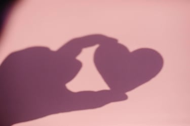 Sur fond rose, ombre d'une main qui tient avec deux doigts un coeur