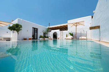 Luxury villa swimming pool with white architecture, turquoise water, and loungers under a blue sky.