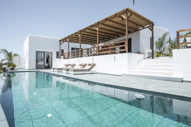 Luxury white villa with a private infinity pool, sun loungers, and a wooden pergola terrace.